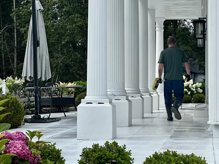 A Nord technician carrying a pump sprayer along the columned portico of a large Simcoe County property, the stone walkway freshly washed
