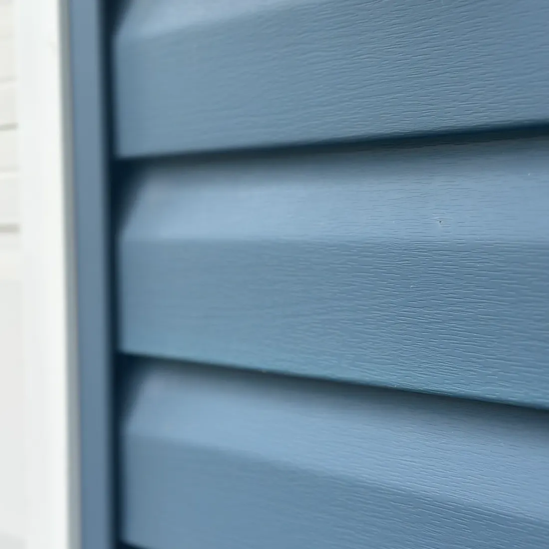 After — Oxidation removal — the chalky UV haze dissolved and hand-brushed off, the original blue back. Same siding, no paint.