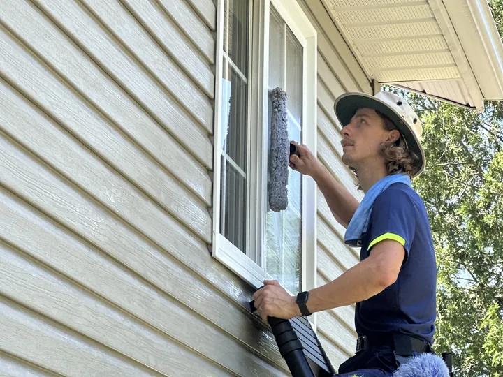 A Nord window cleaner running a soaked scrubber across a pane of glass, the sheet of water still on the window before the squeegee pass