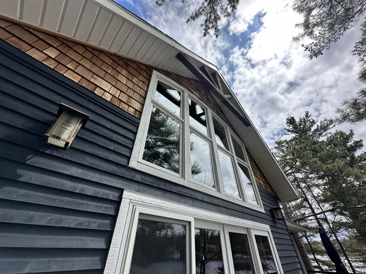 A dark-sided lake house rising to a tall arched window wall under cedar shakes
