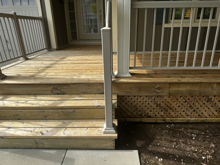 A porch and its steps after a wood-safe wash, the boards back to a clean warm brown against a white post and lattice
