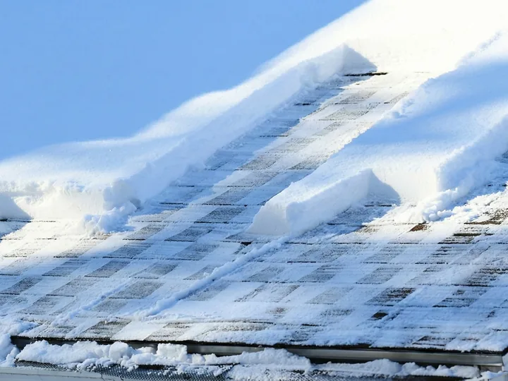 Deep snow slabbed across an asphalt-shingle roof, breaking away in blocks along the slope