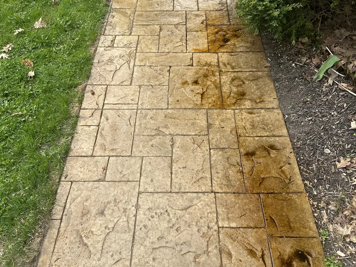 A stamped concrete walkway marked with orange-brown rust stains bleeding across several slabs
