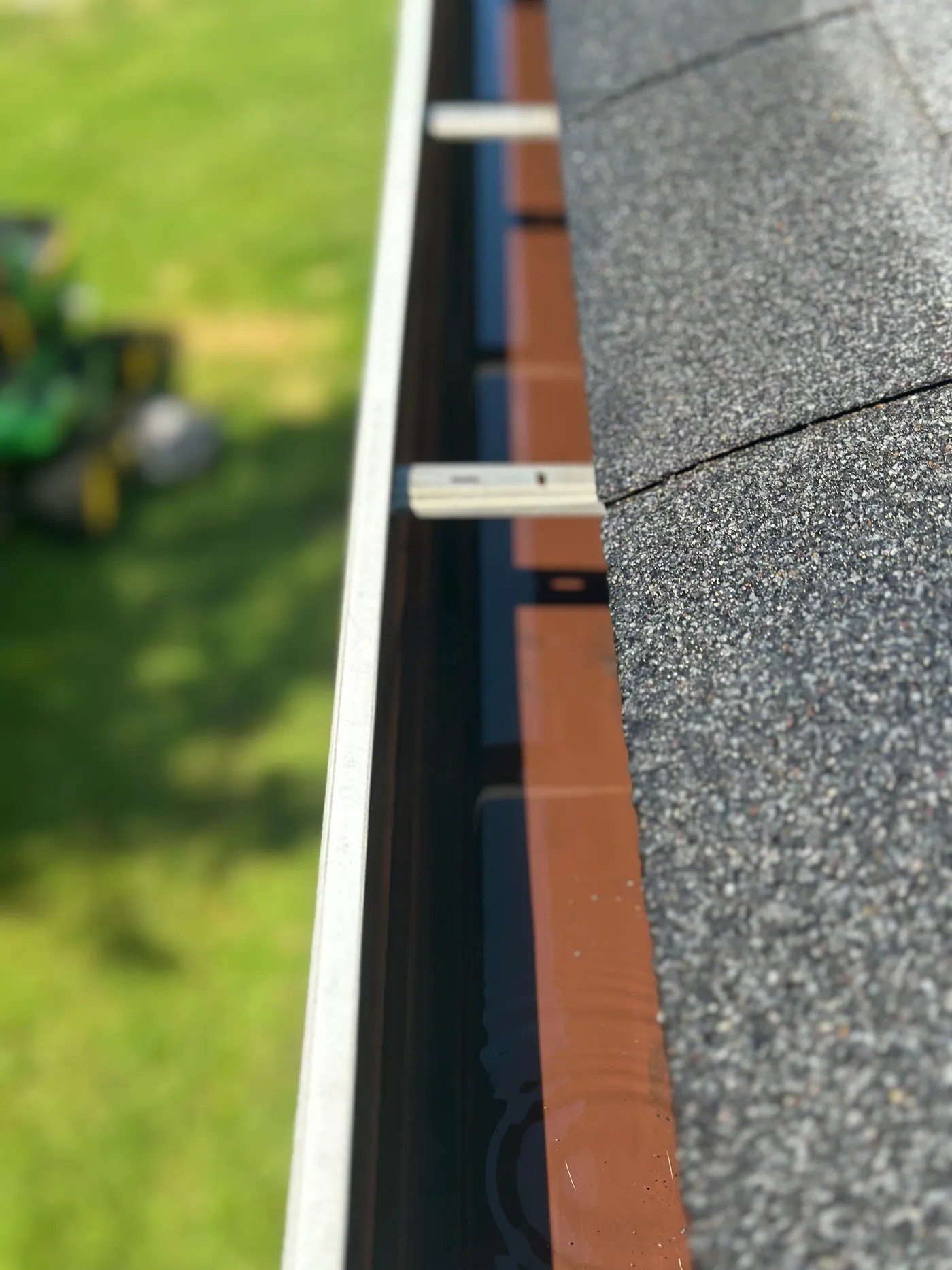 Looking down the inside of a freshly cleared eavestrough — the trough empty and clean, sunlit lawn below