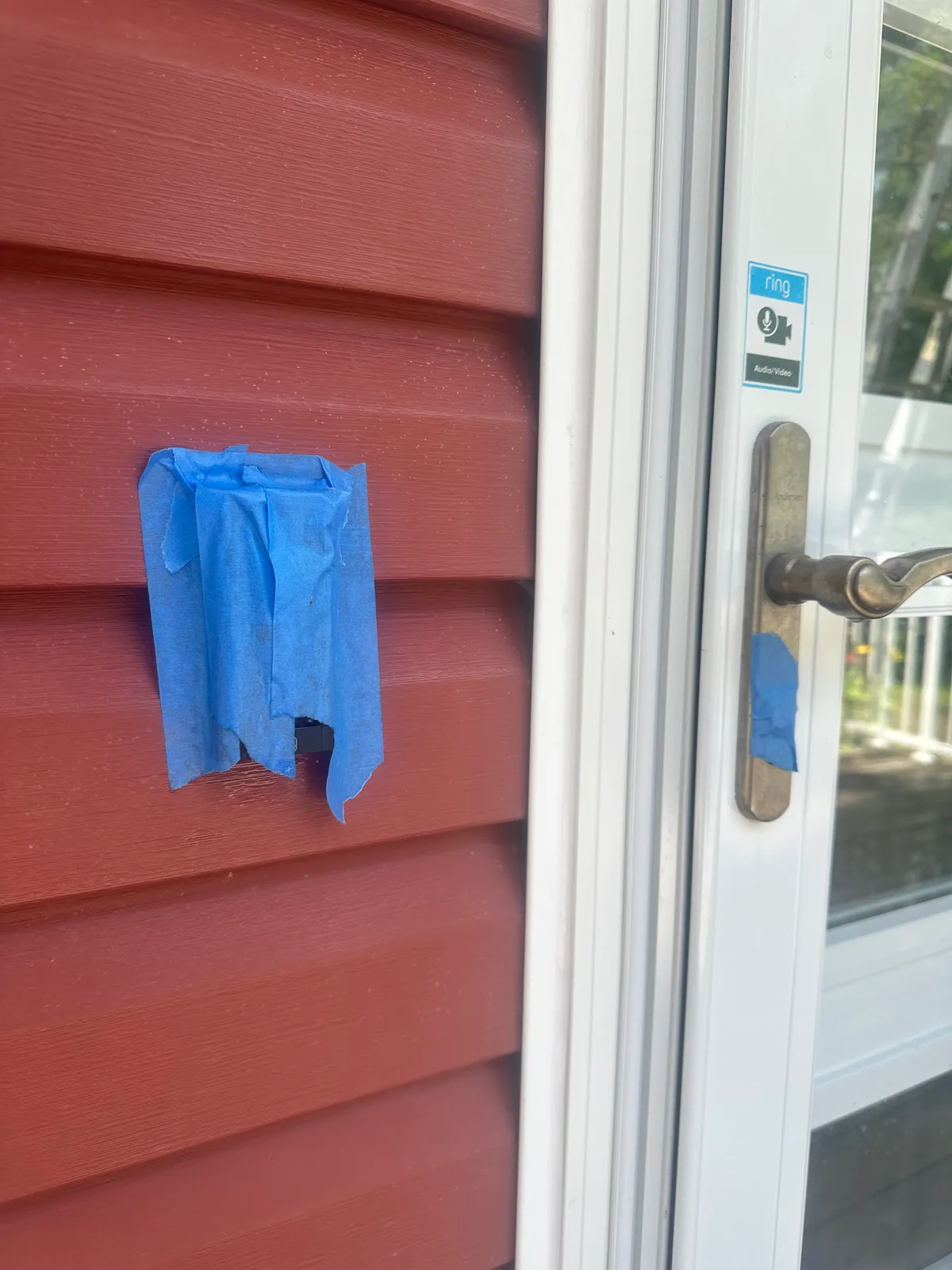Blue painter’s tape sealing an outdoor electrical outlet on red siding, with the door lock beside it taped over too, before a soft wash begins