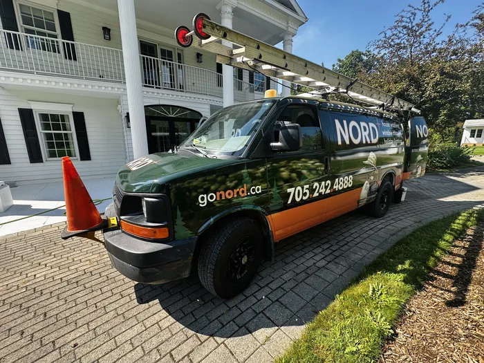 The Nord van parked on the drive of a large white home, ladders racked on the roof and the gonord.ca phone number along the side