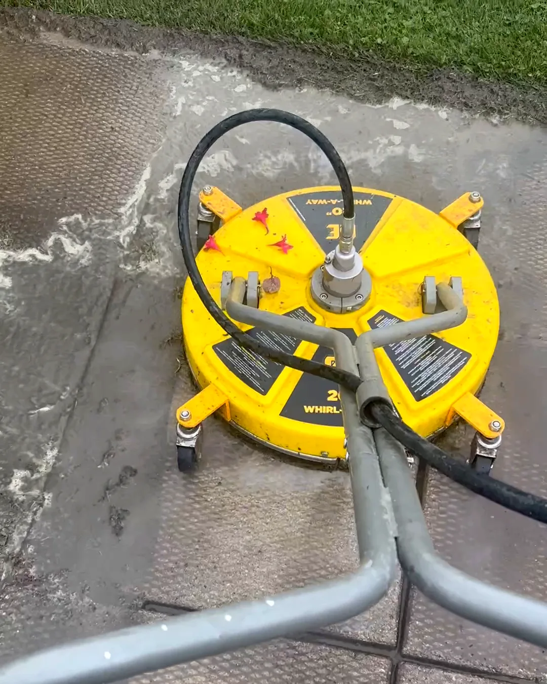 A Nord surface cleaner mid-pass across a concrete patio, seen over the operator’s handlebars